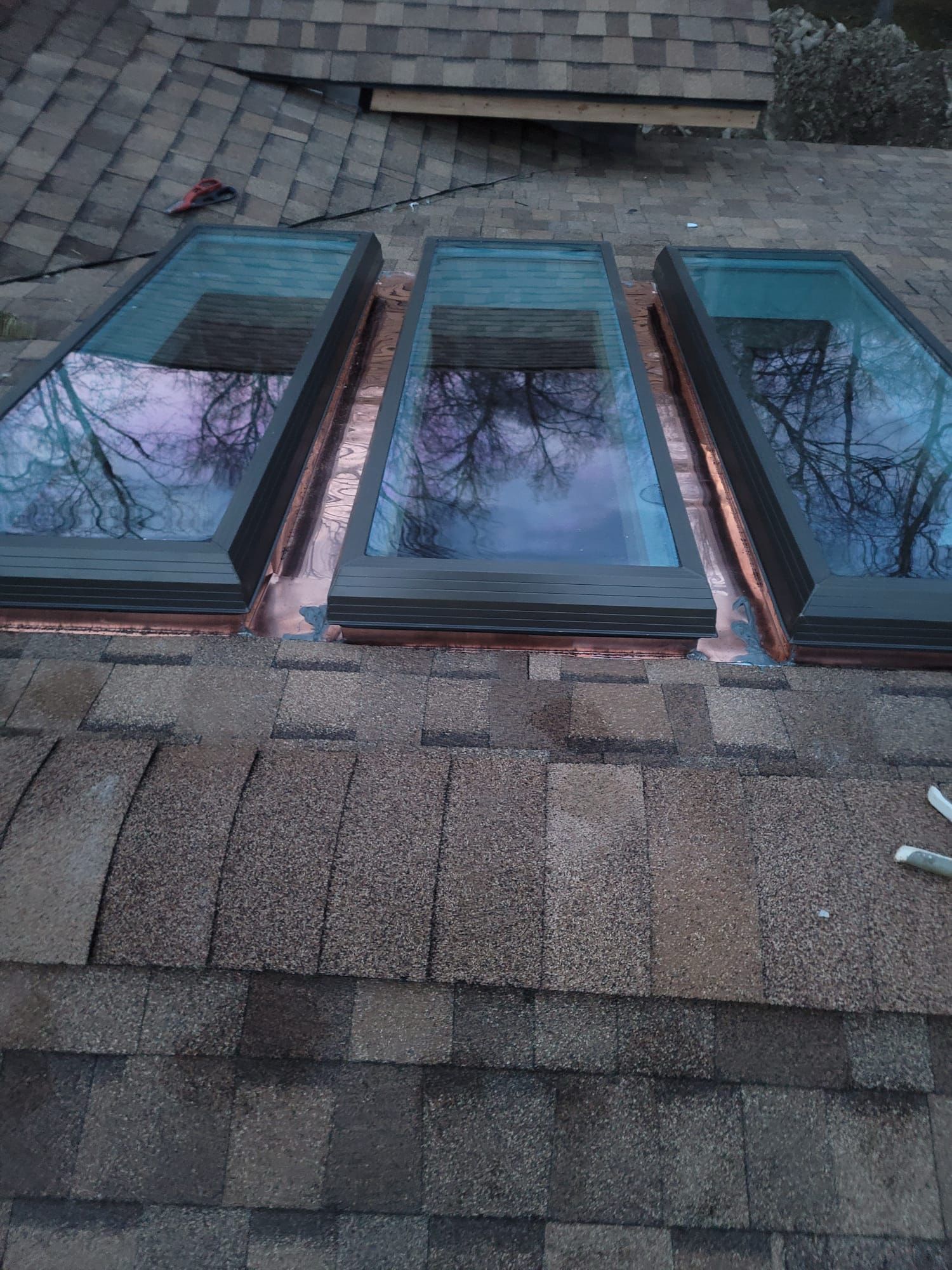 Three rectangular skylights installed on a shingled roof, with copper flashing.