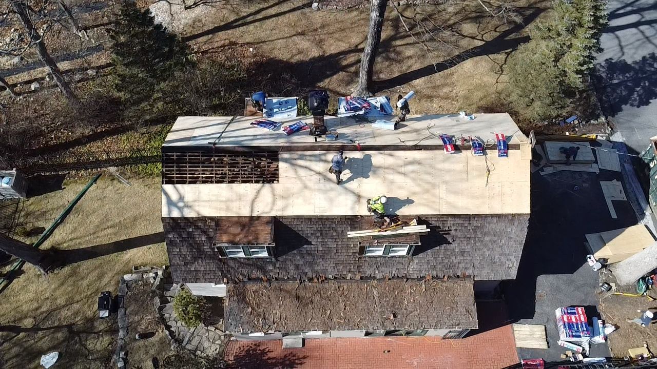 Overhead view of roofers replacing a roof. Partially shingled roof with workers, equipment, and a bare section.