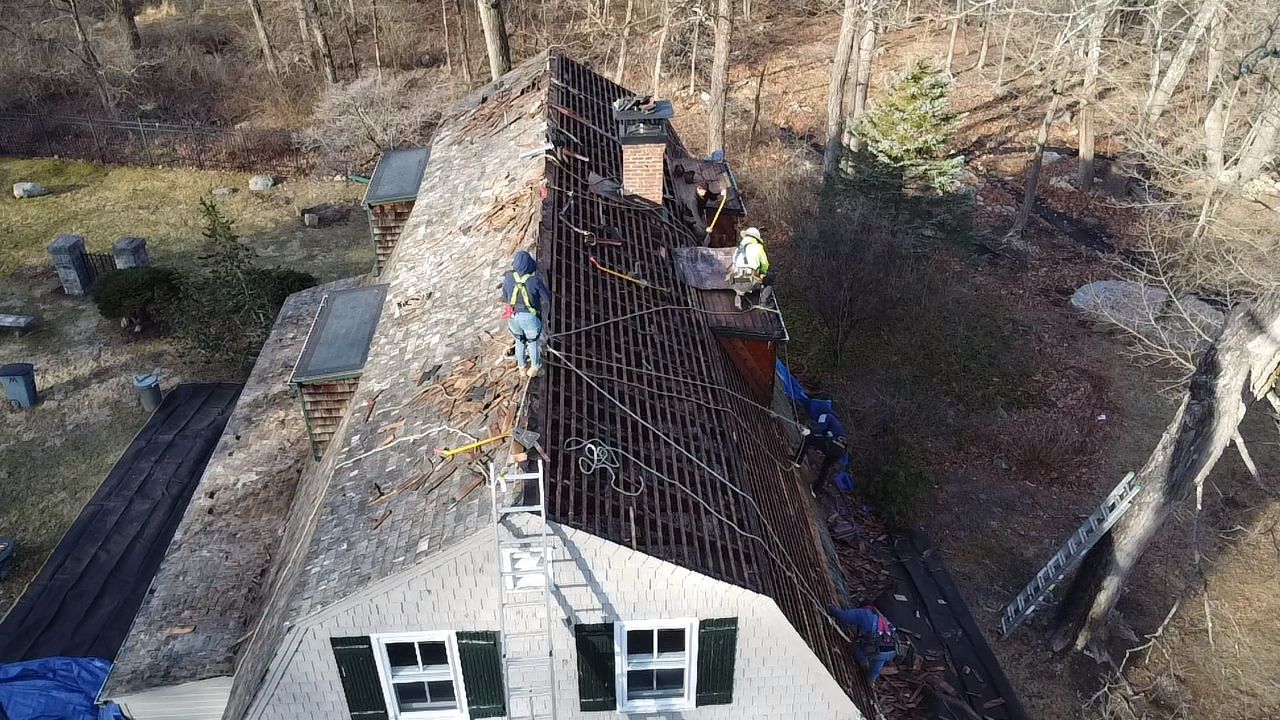 Roof partially stripped, revealing underlying structure. Workers on the roof.  Daytime, outdoor setting.