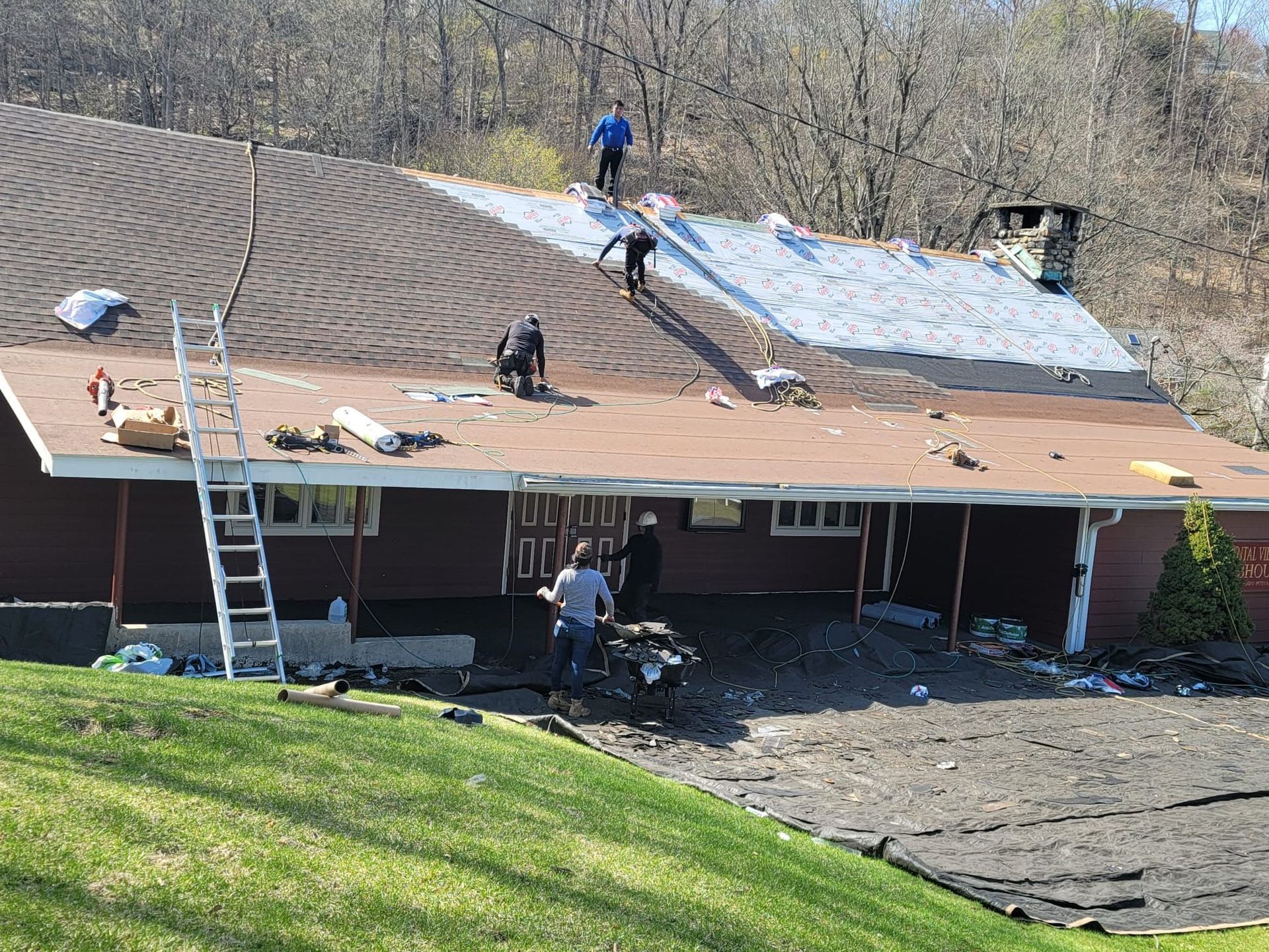 Roofers working on a house, partially removing old shingles. Sunny day, ladder visible.