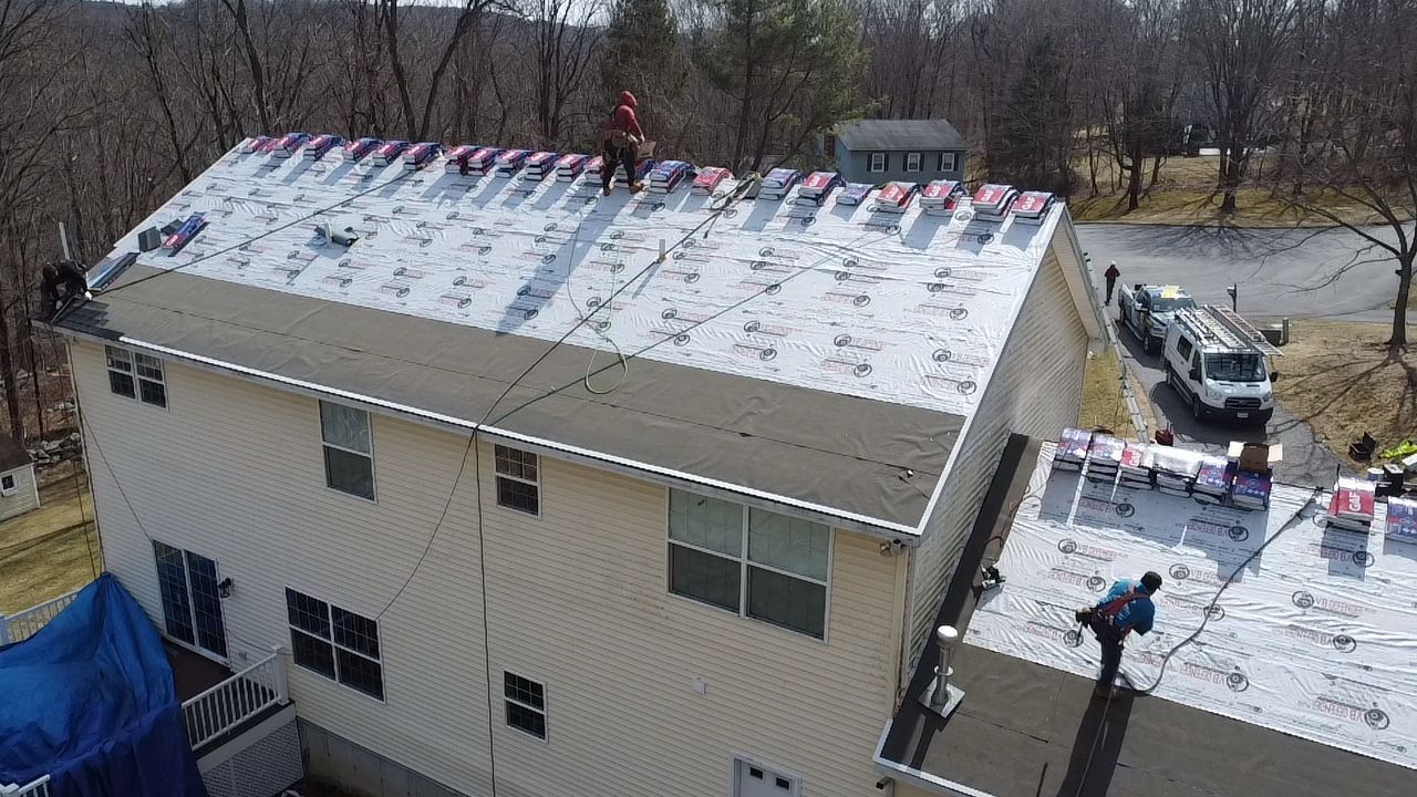 Roofers working on a residential roof, removing old shingles and installing new ones on a sunny day.