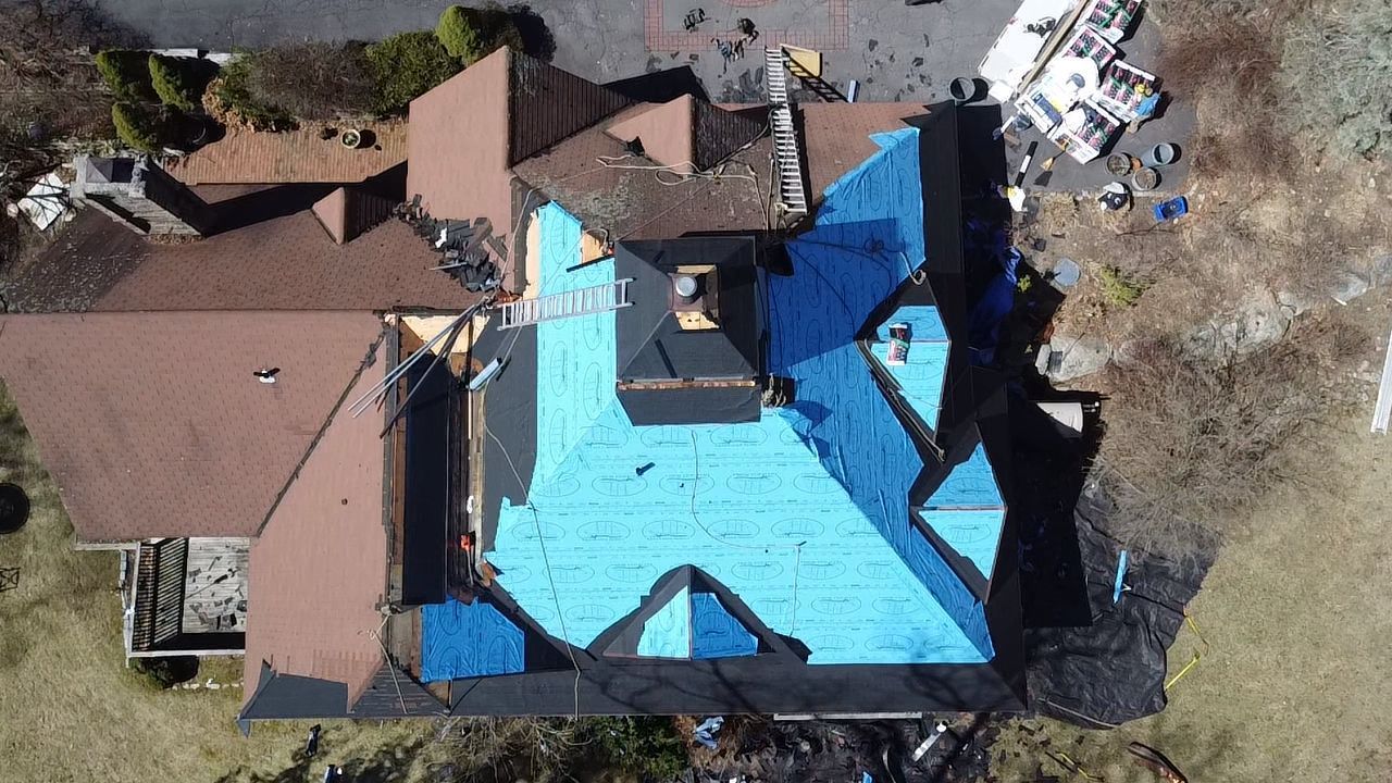 Overhead view of a house roof partially covered in blue tarp, brown shingles and debris.