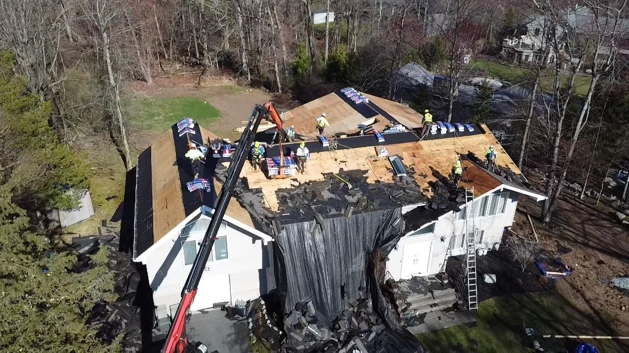Roofers working on a house with a damaged roof; crane lifting materials.