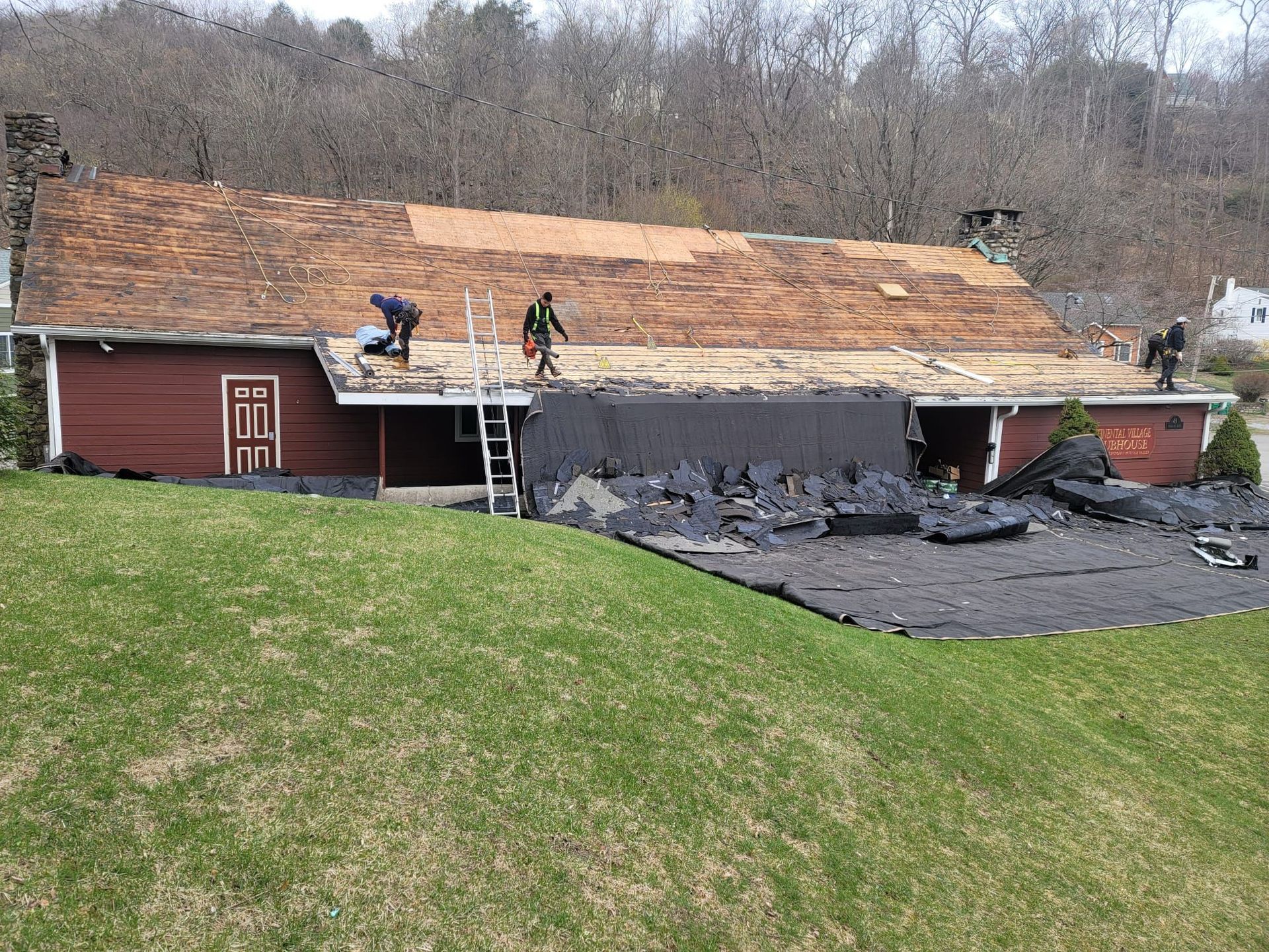 Roofers working on a red house, removing old shingles and replacing them.