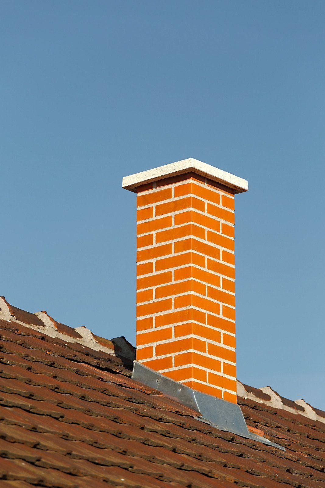 Brick chimney on a red tile roof against a blue sky.