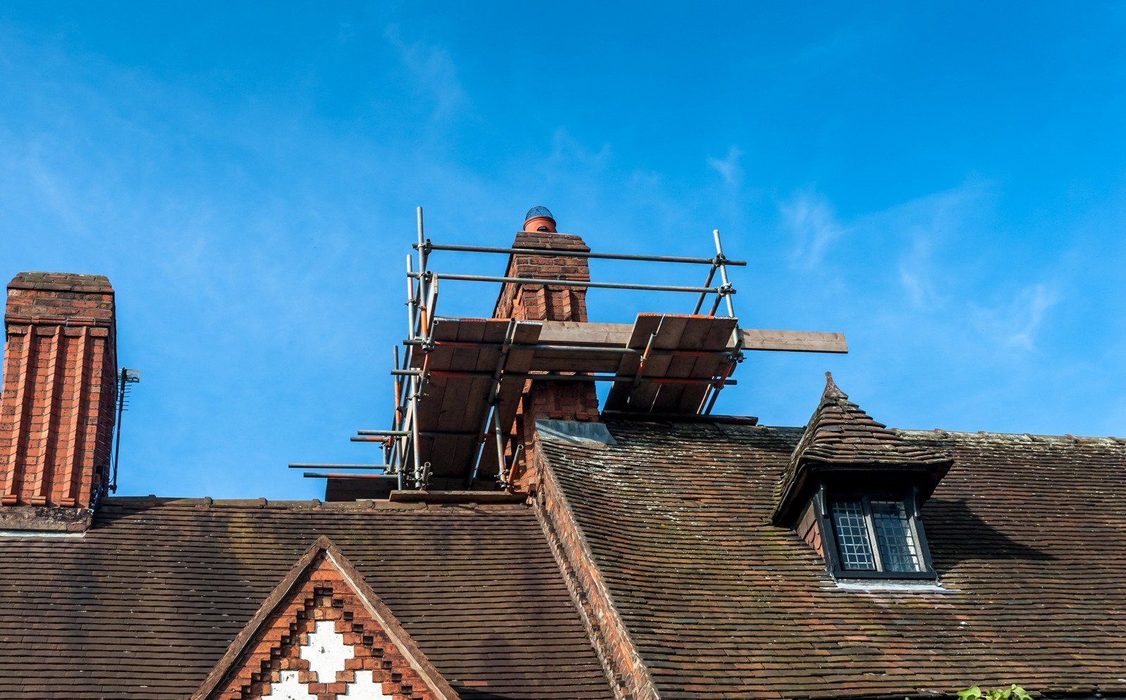 Brick chimneys on a roof, scaffolding for repair work under a blue sky.