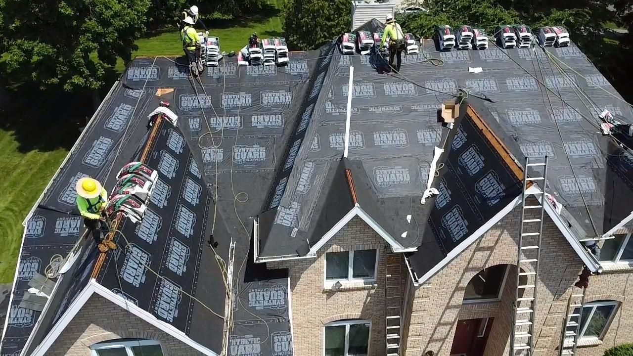 Roofers working on a residential roof, laying down shingles.