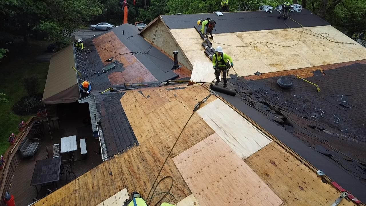 Roofers in safety gear work on a roof, replacing shingles.