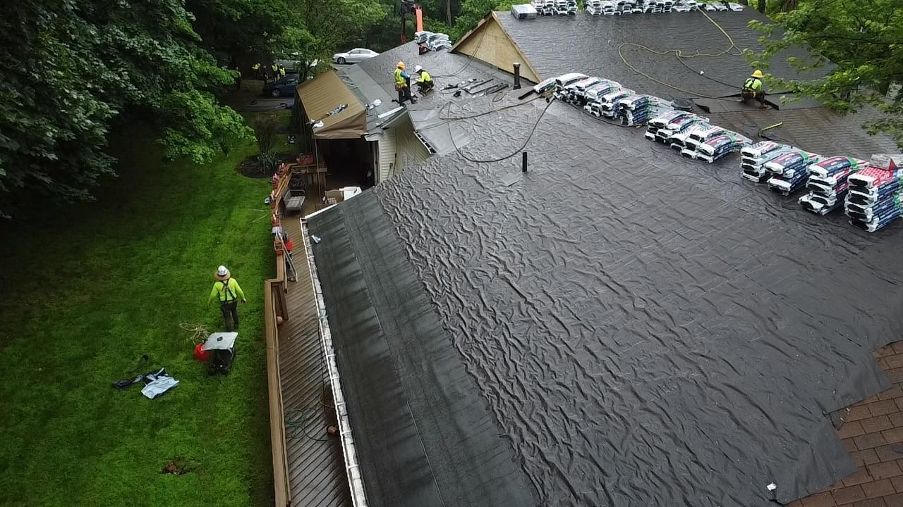 Roof with workers, shingles, and green lawn.