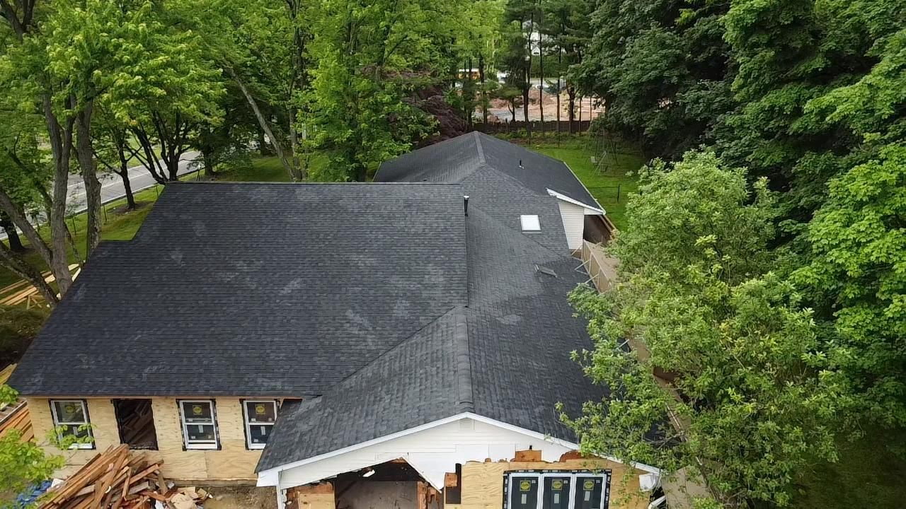 Overhead view of a house with a dark gray shingled roof, surrounded by green trees.