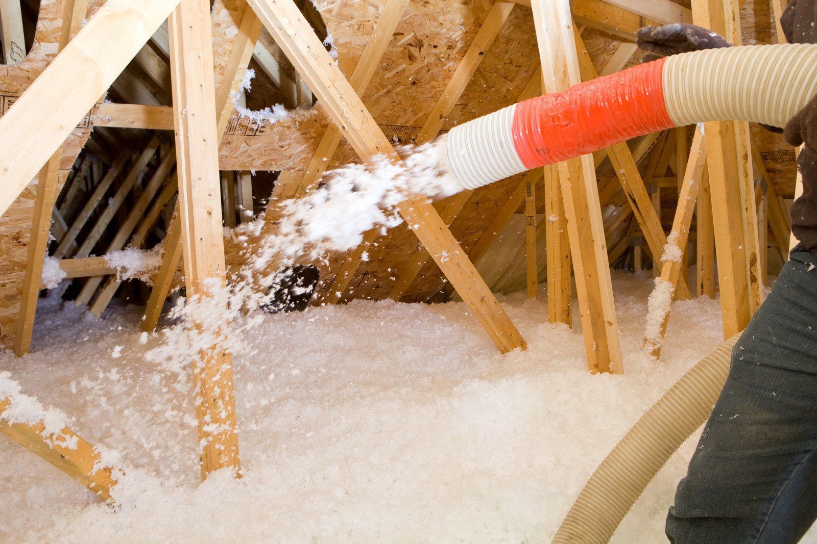 Person blowing insulation into an attic, using a hose.