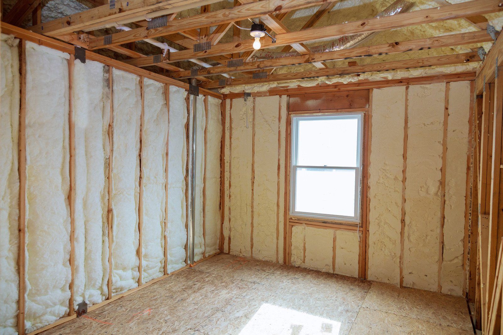 Interior room under construction, with exposed wooden beams, insulation between studs, and a window.