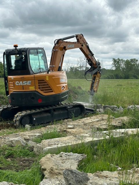 A case excavator is breaking rocks in a field.