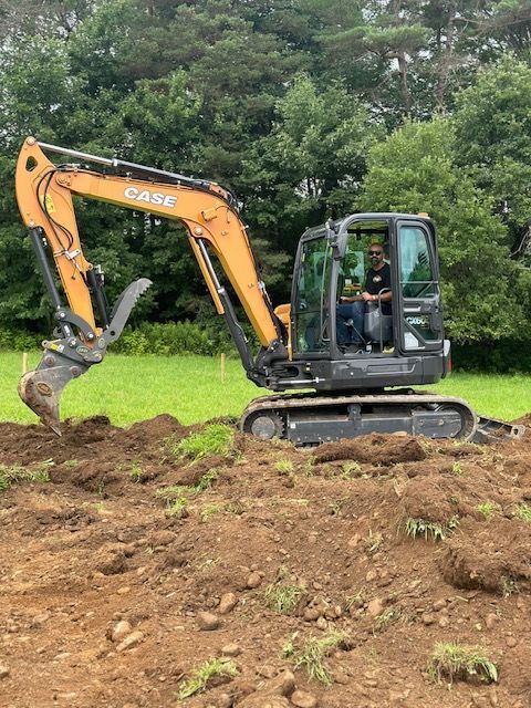 A man is driving an excavator in a dirt field.