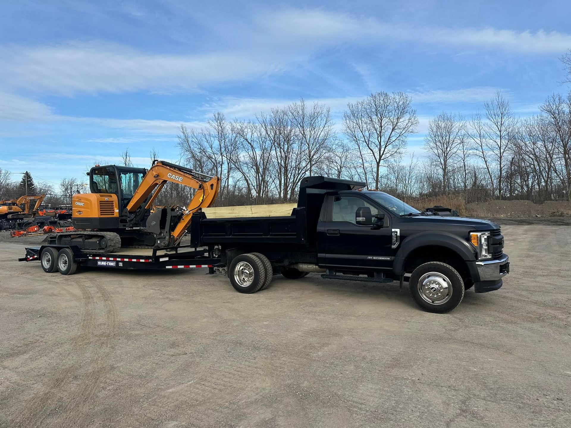 A black truck is towing a yellow excavator on a trailer.
