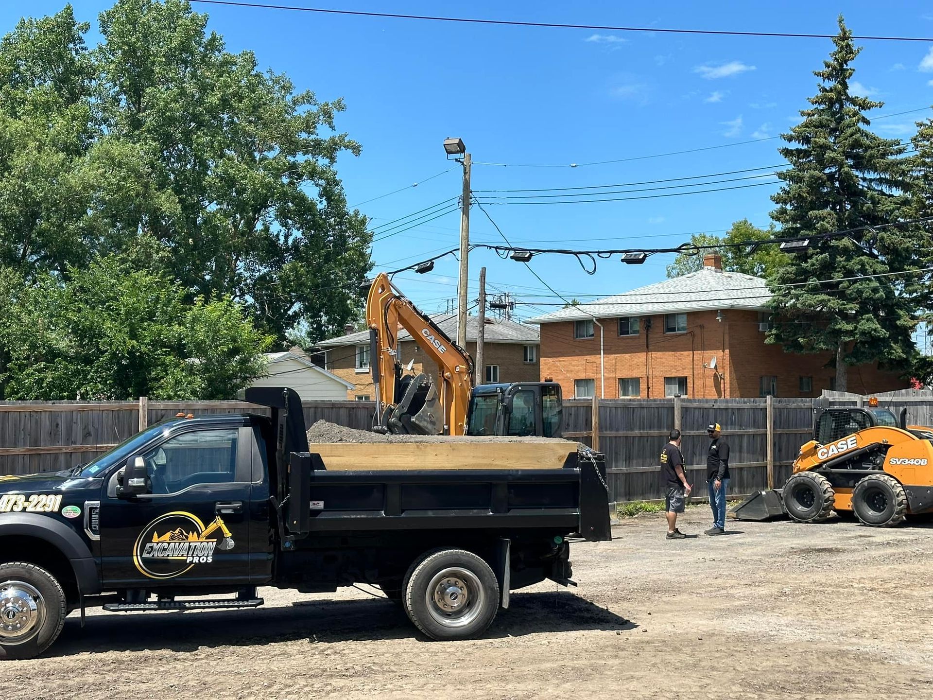 A dump truck is parked in a dirt lot next to an excavator.