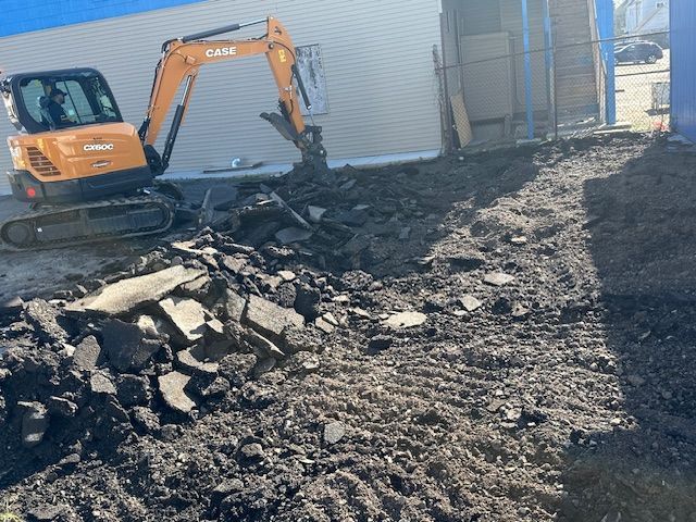 An excavator is digging a hole in the dirt in front of a building.