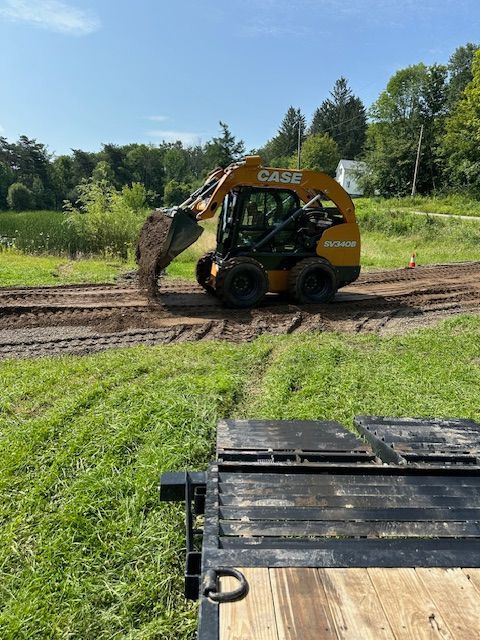 A bulldozer is moving dirt in a field next to a trailer.
