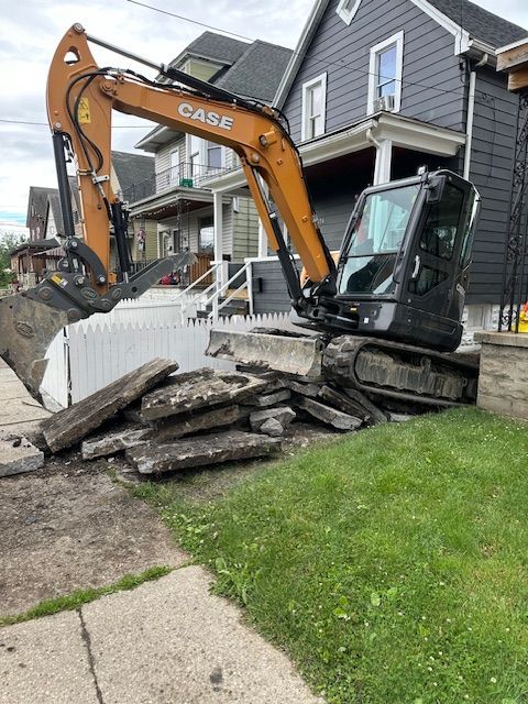 A case excavator is working on a sidewalk in front of a house.