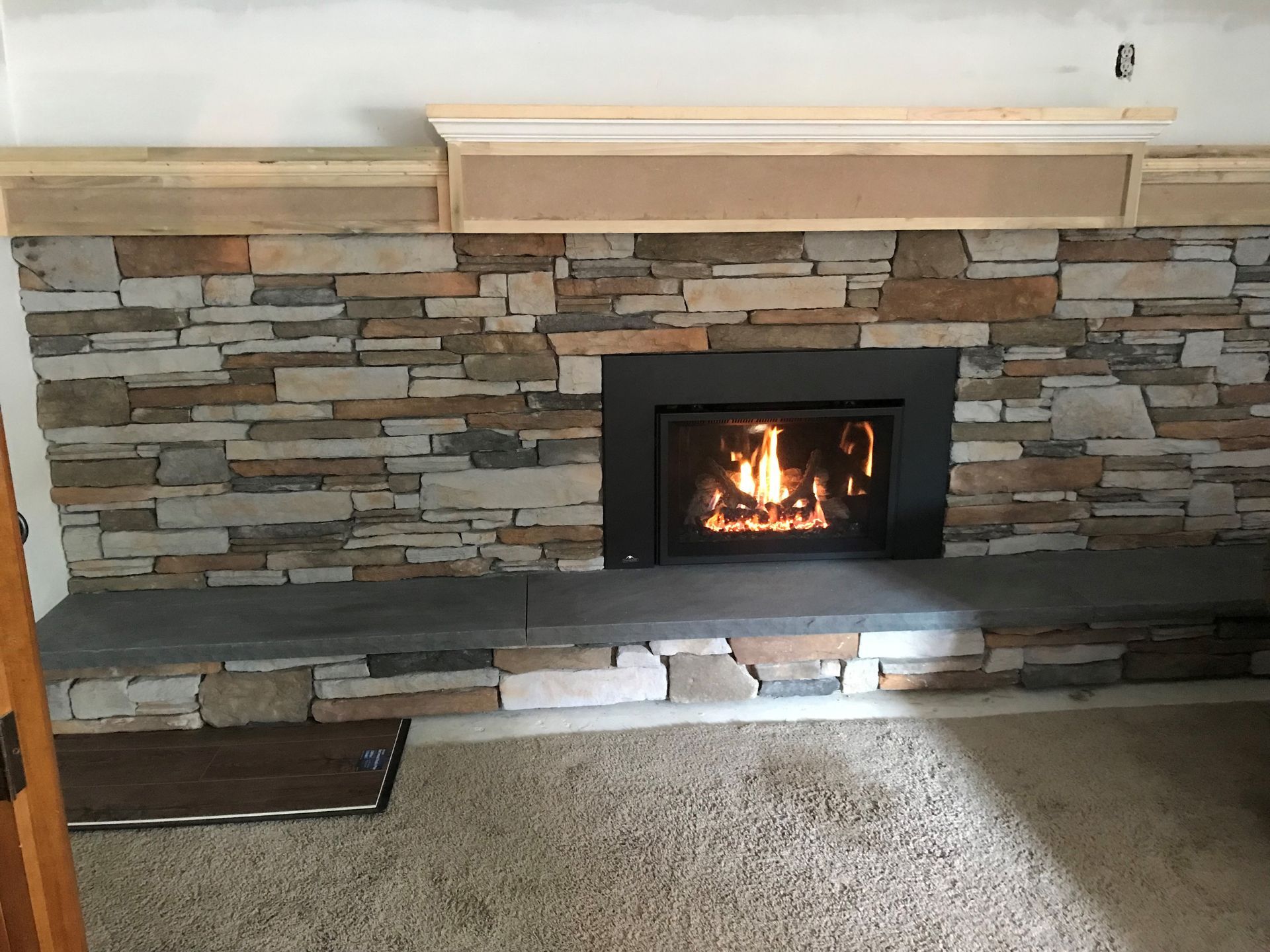 A fireplace with a stone wall and a wooden mantle in a living room.