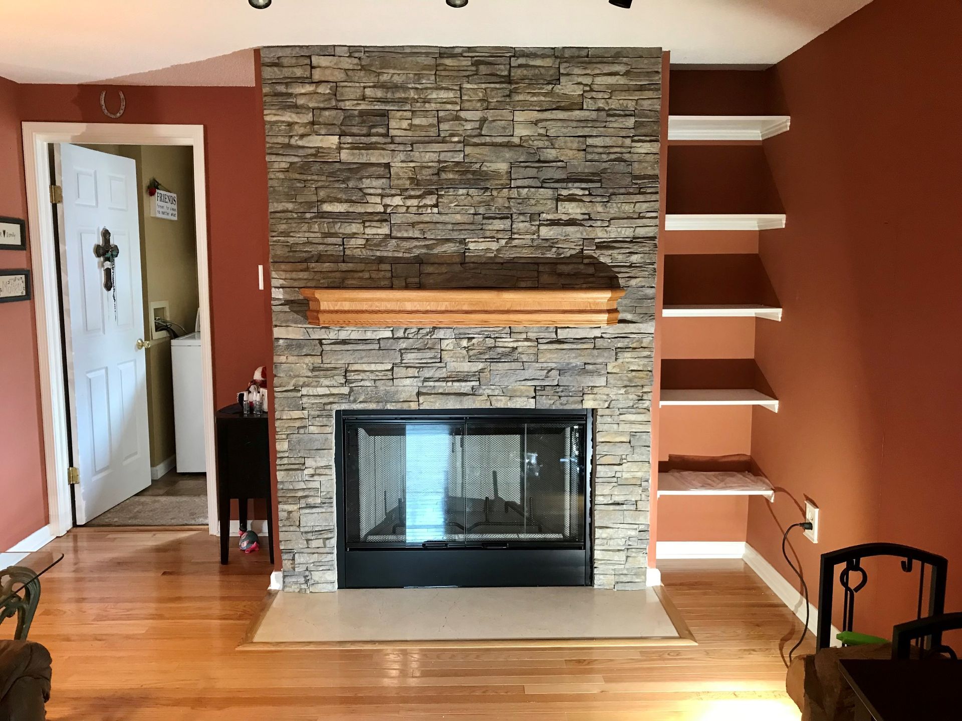 A living room with a stone fireplace and shelves.