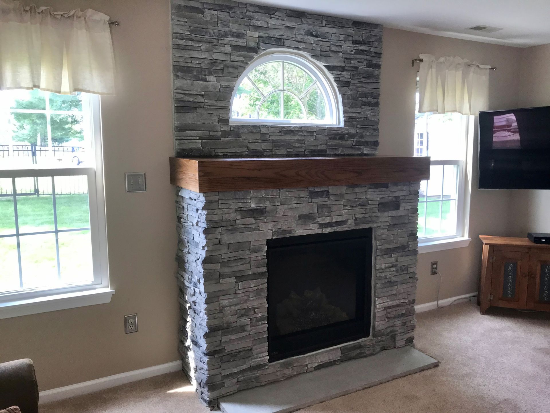 A living room with a stone fireplace and a flat-screen TV.