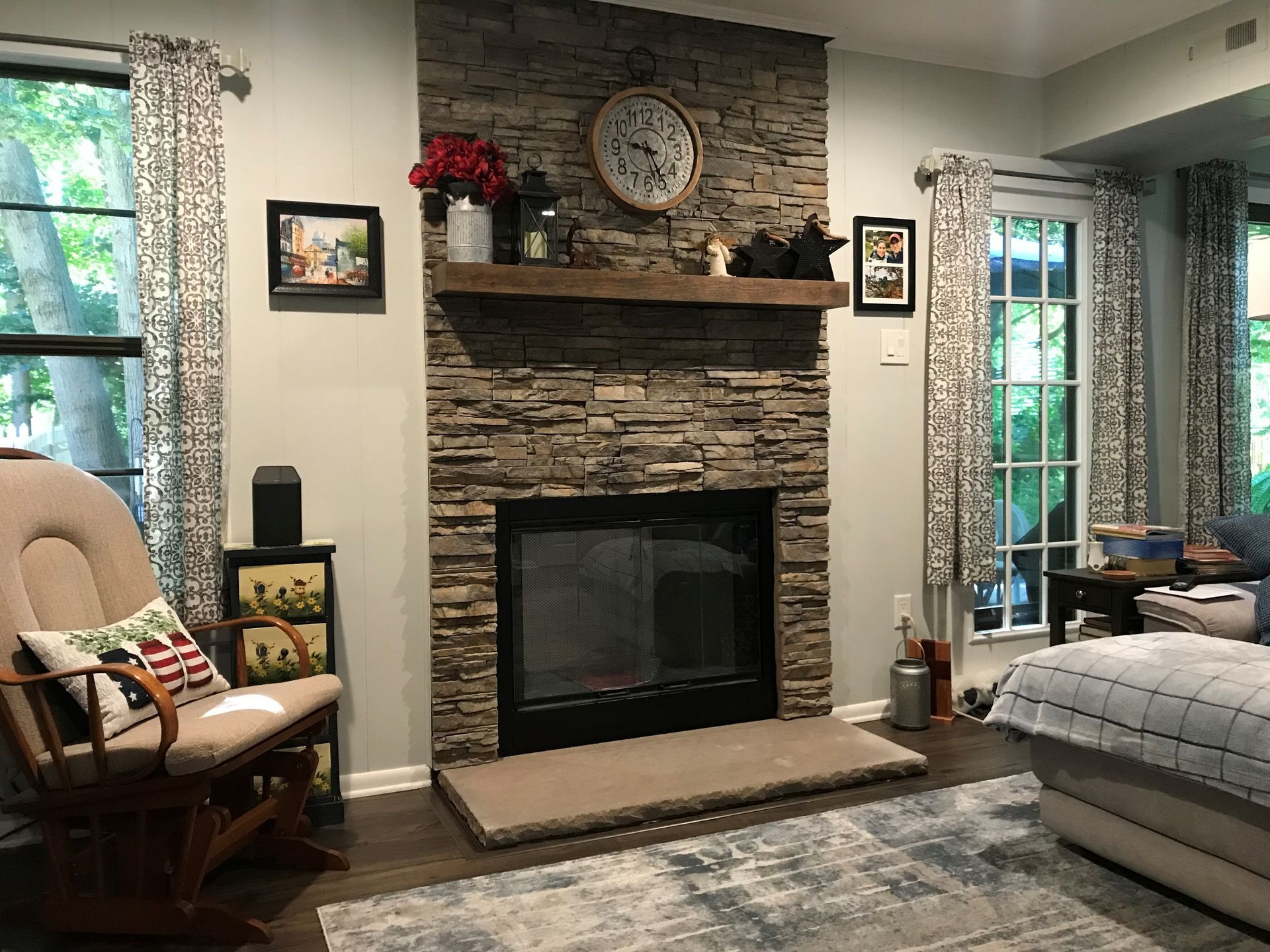 A living room with a stone fireplace and a clock on the mantle.