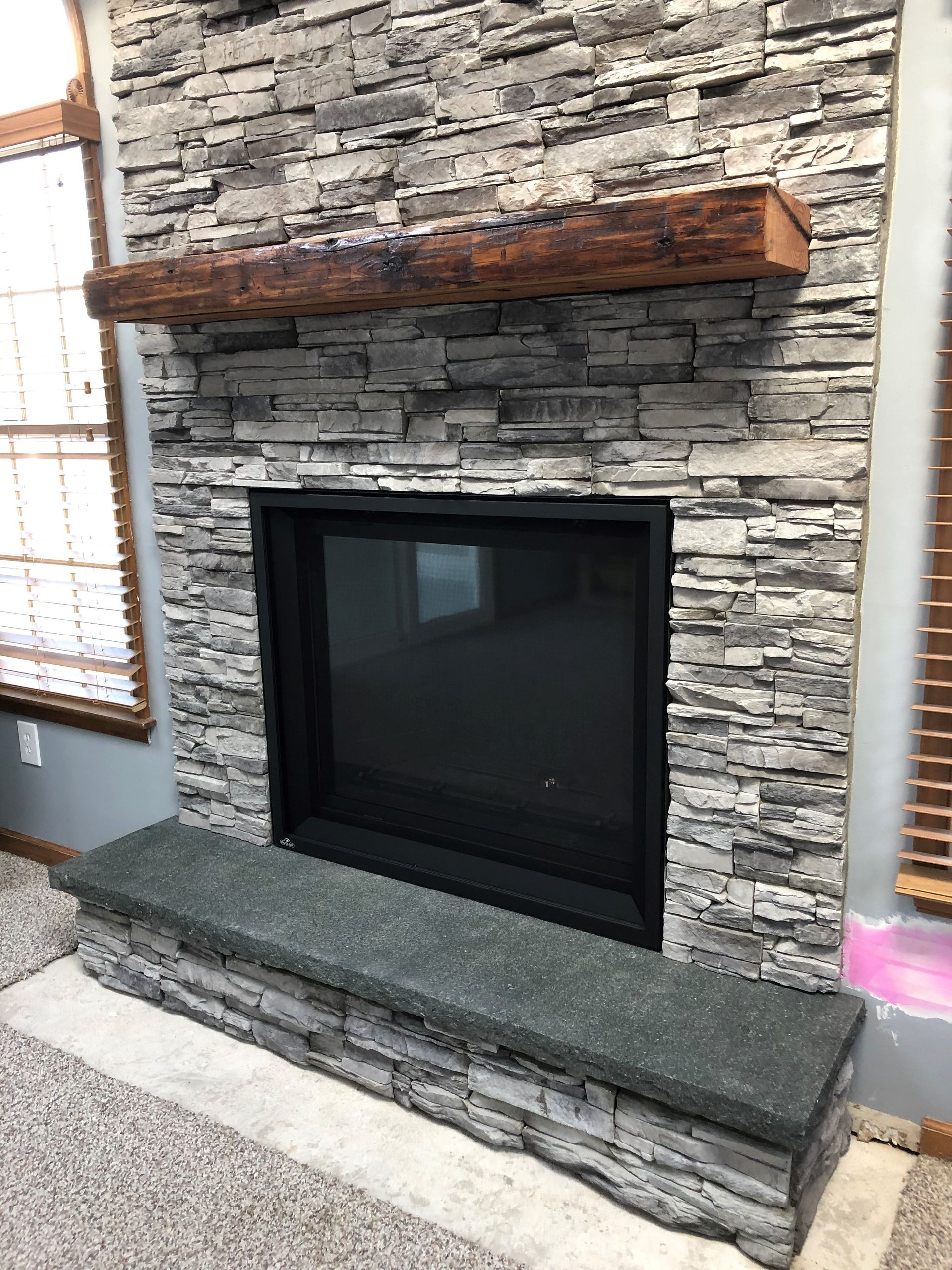 A fireplace with a stone wall and a wooden mantle in a living room.