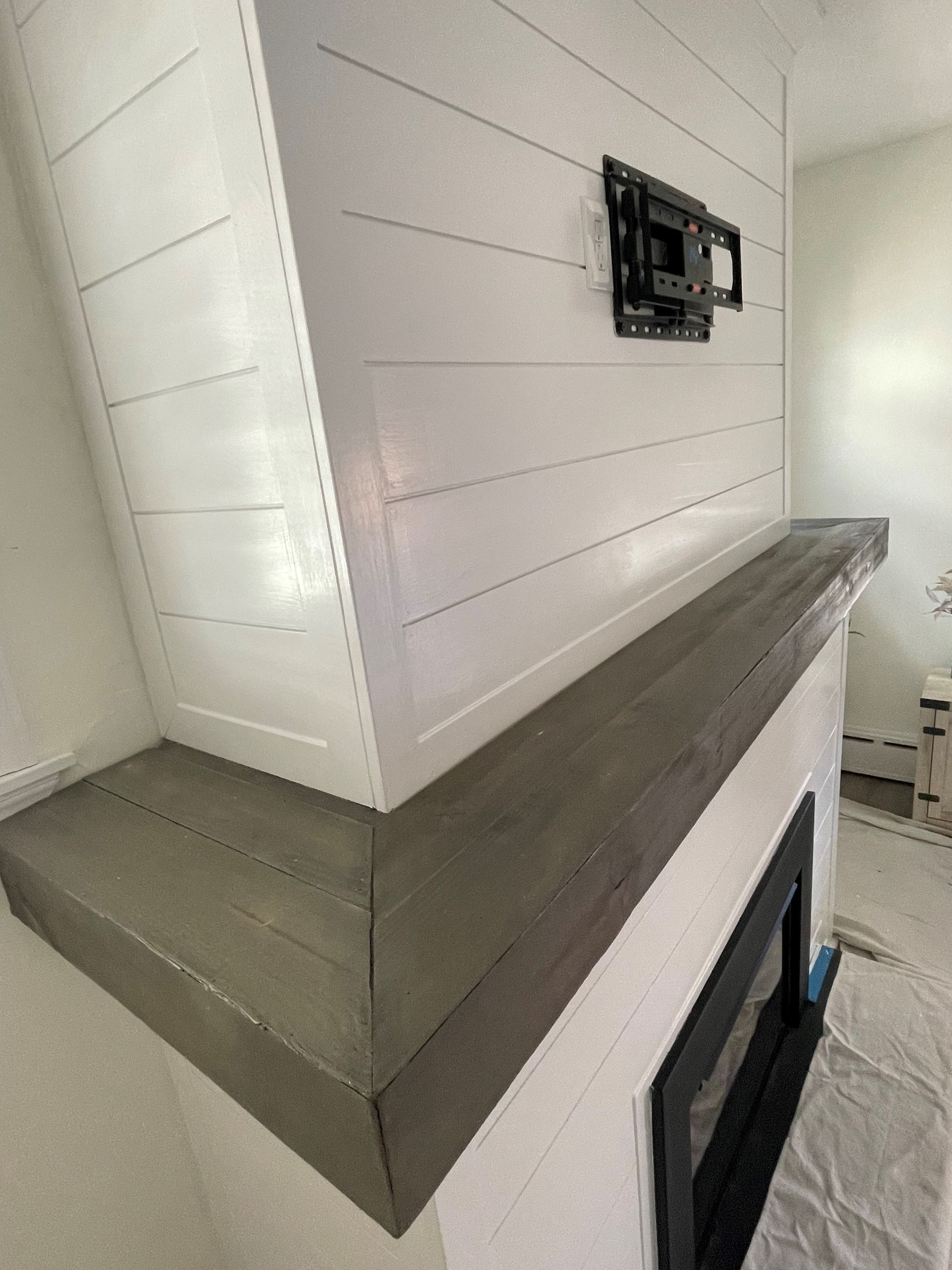 A fireplace with a wooden mantle and a flat-screen TV mounted on the wall.