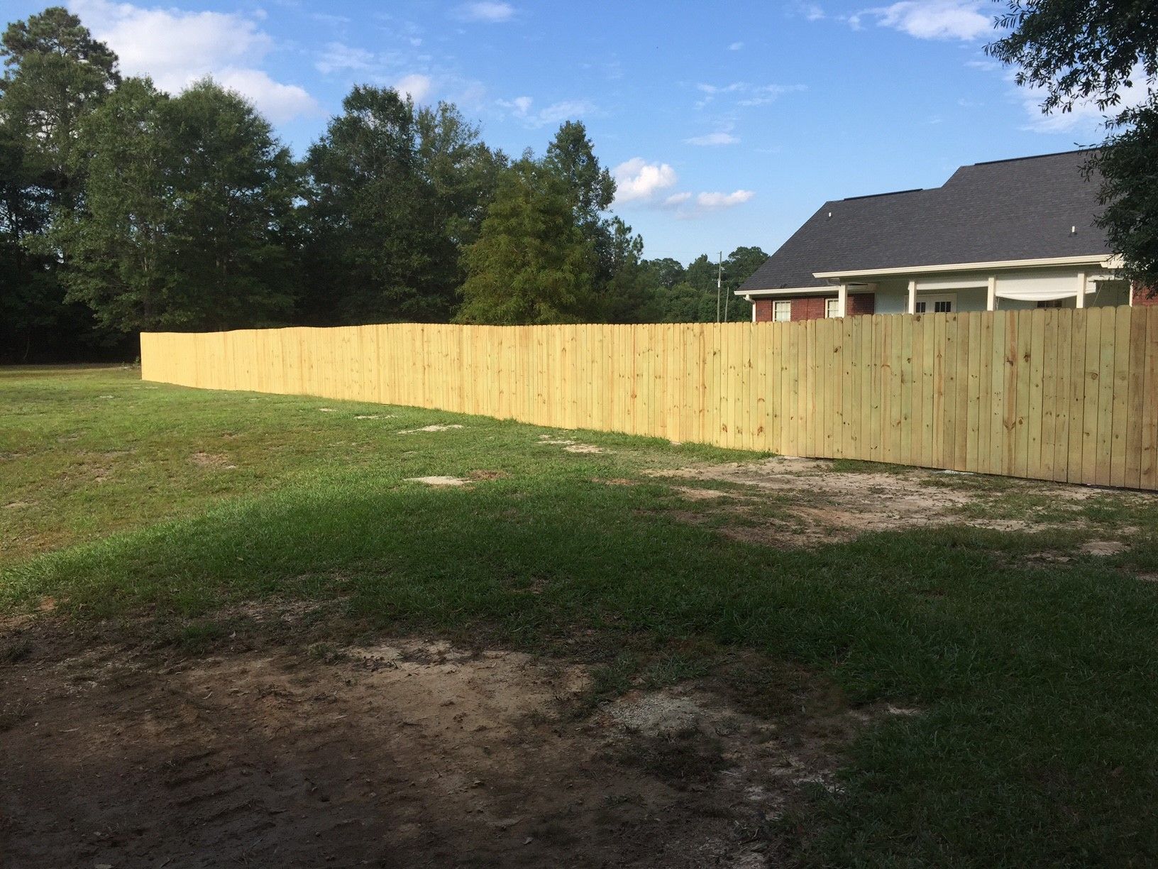 Long wooden fence along a grassy backyard beside a house under a blue sky.