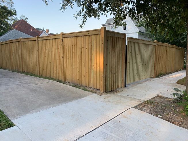 Wooden privacy fence along a concrete driveway at a residential corner lot.