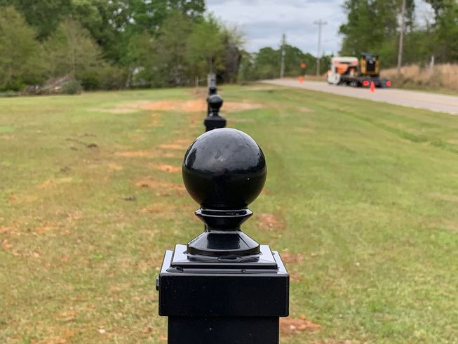 Black decorative post in foreground on grassy roadside with workers and truck in the distance