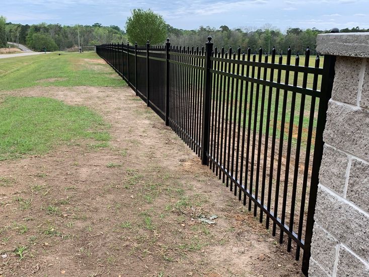 Black metal fence beside a grassy dirt path next to a stone wall in a park