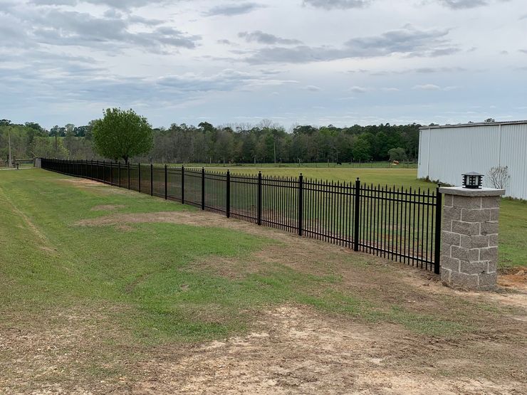 Black metal fence along grassy field beside a stone post under a cloudy sky