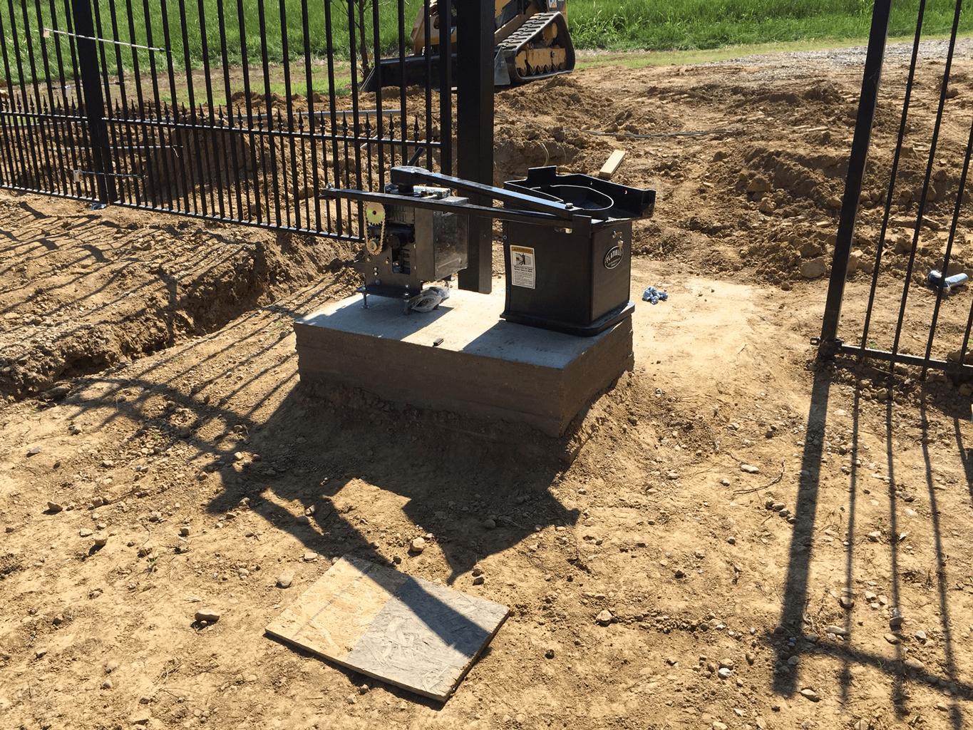 Concrete platform with fenced outdoor equipment and a metal gate in a dirt area.