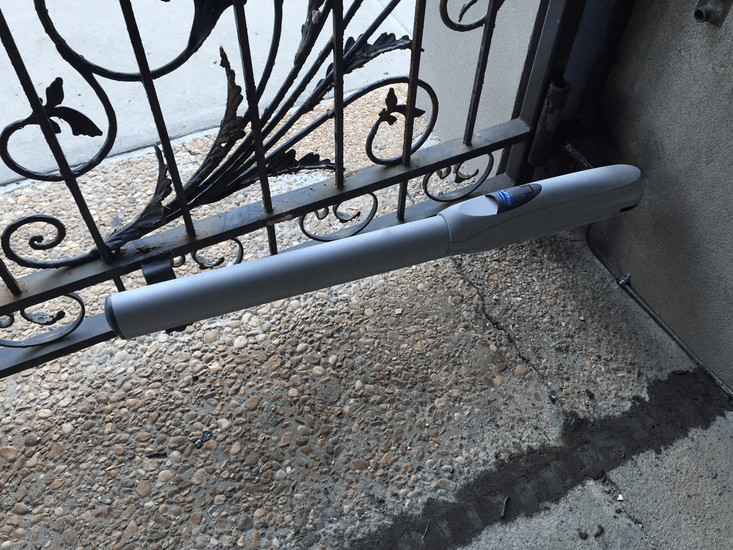 Gray cylindrical barrier leaning against a black wrought-iron gate on a rough concrete step