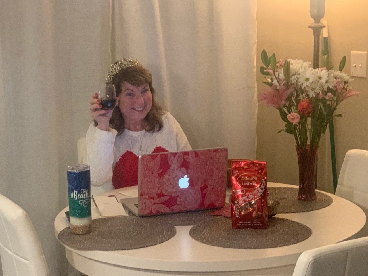 A woman is sitting at a table with a laptop and a glass of wine.