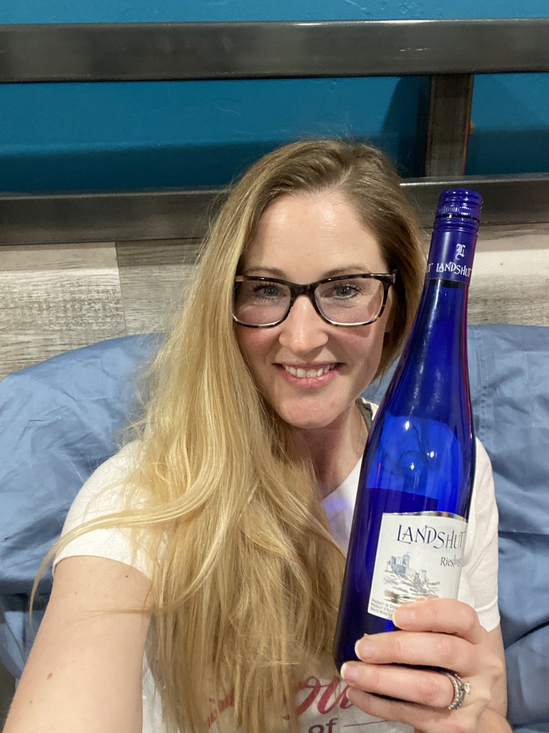 A woman wearing glasses is holding a bottle of wine.