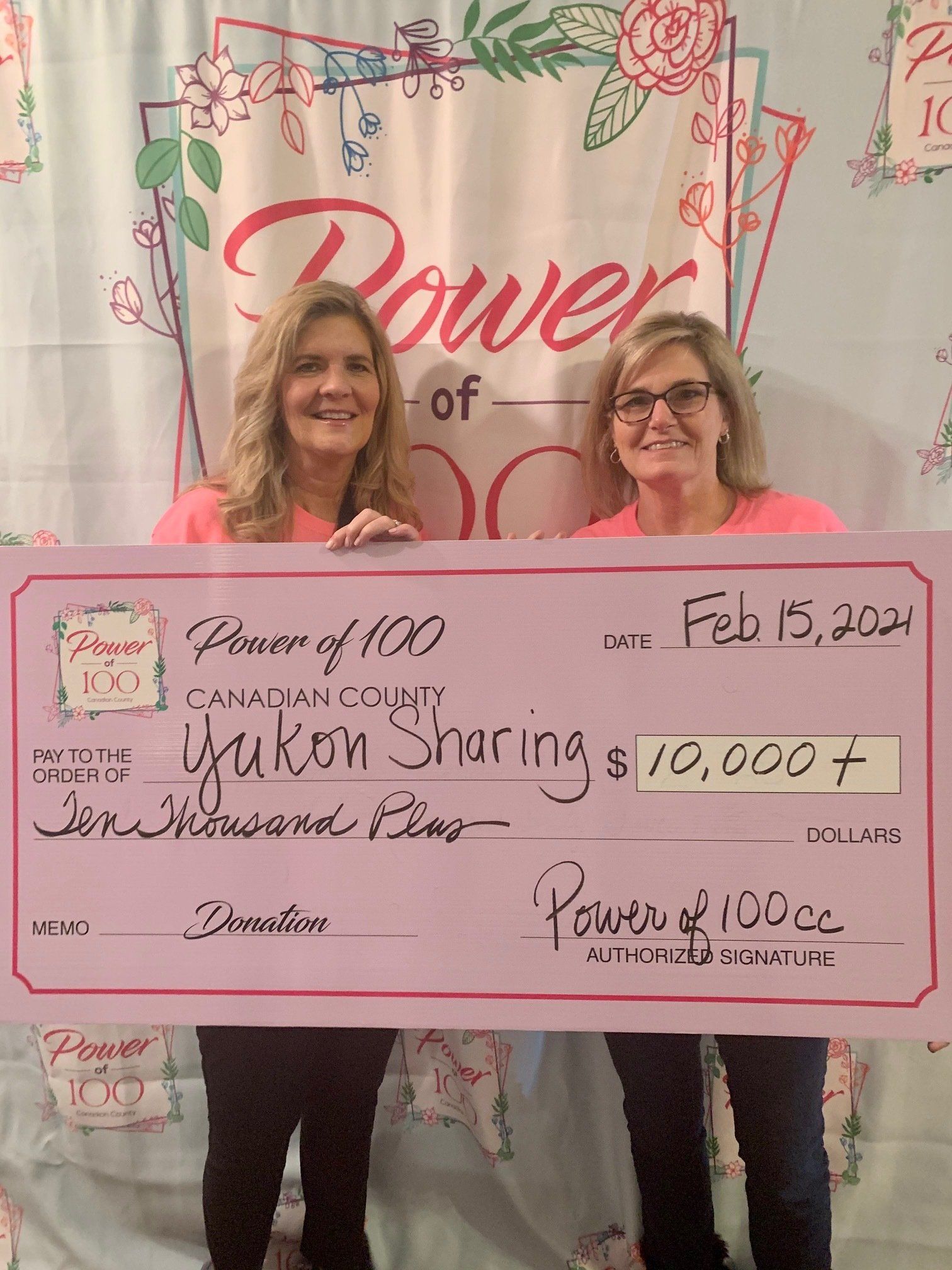 Two women are standing next to each other holding a large pink check.