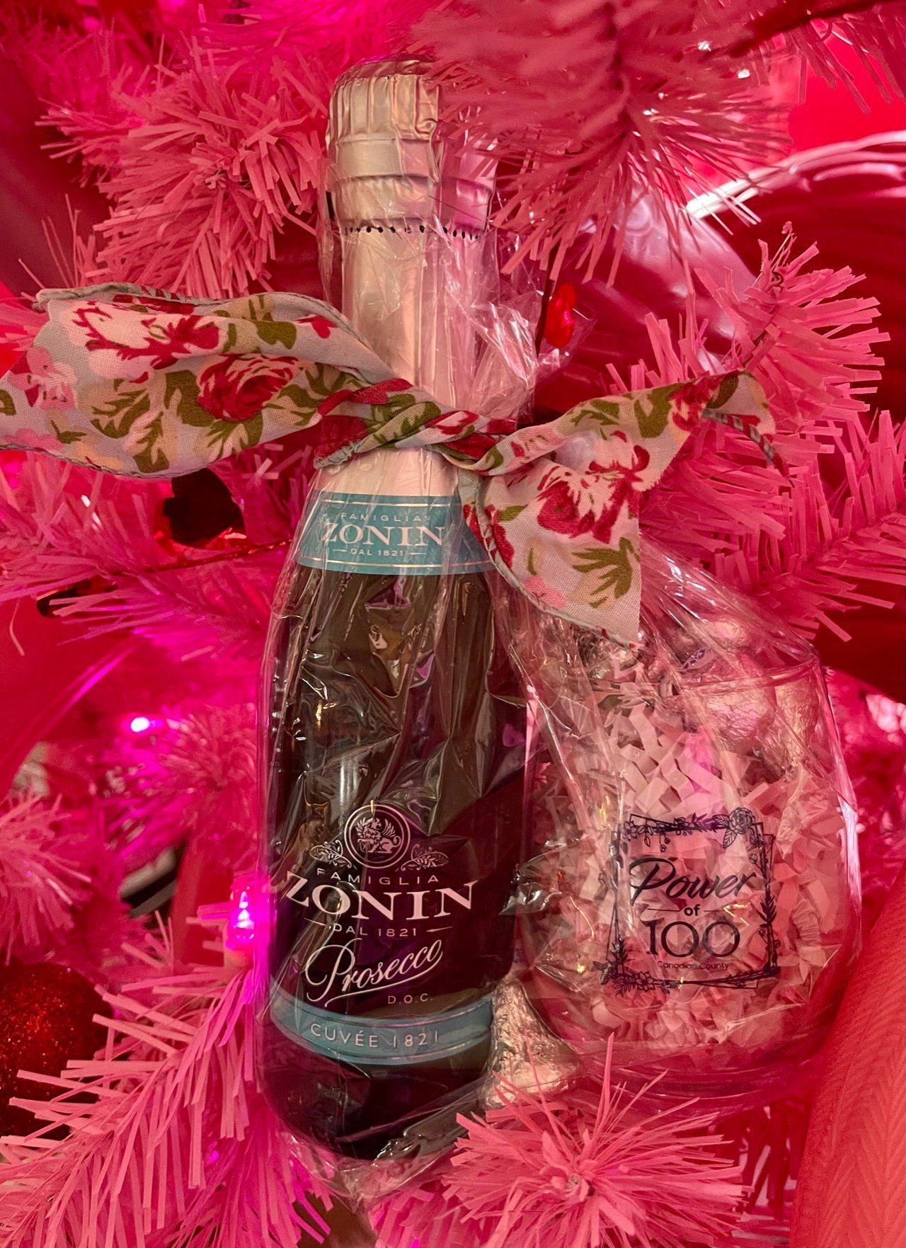 A bottle of wine is sitting on top of a pink christmas tree.