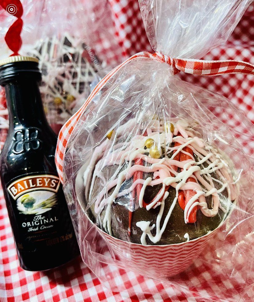 A bottle of bailey 's next to a chocolate donut wrapped in plastic.