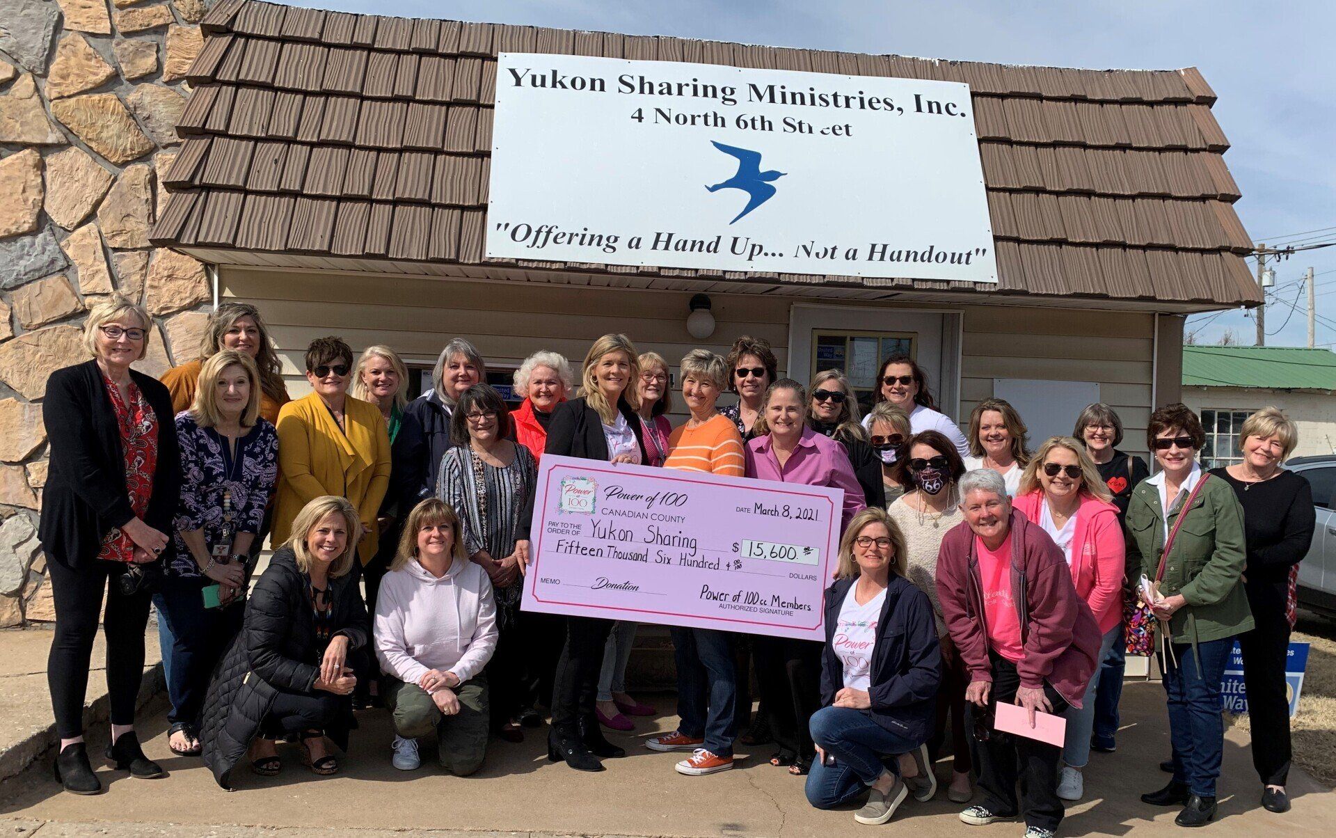 A group of women are standing in front of a building holding a large check.