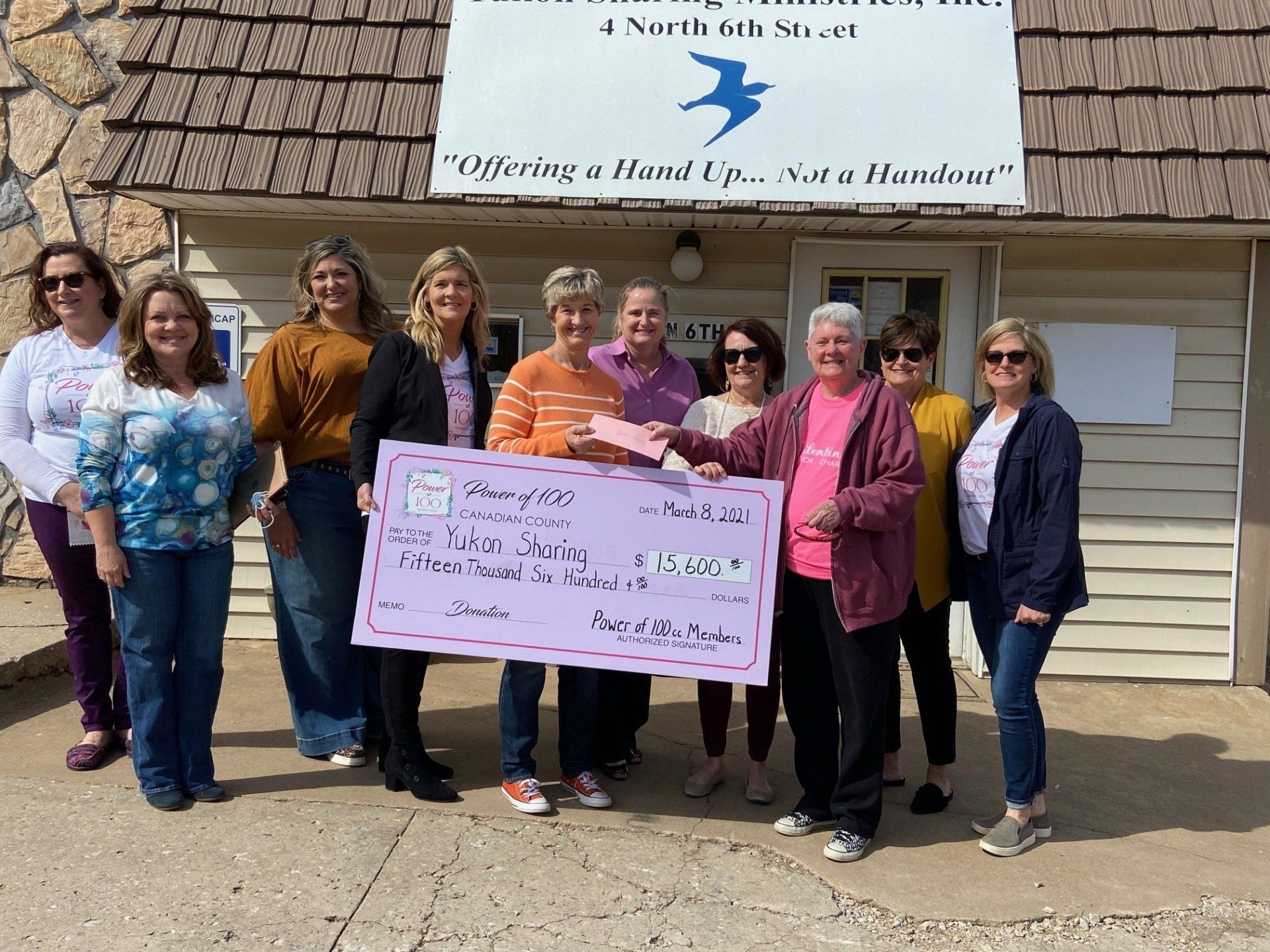 A group of women standing in front of a building holding a large check.