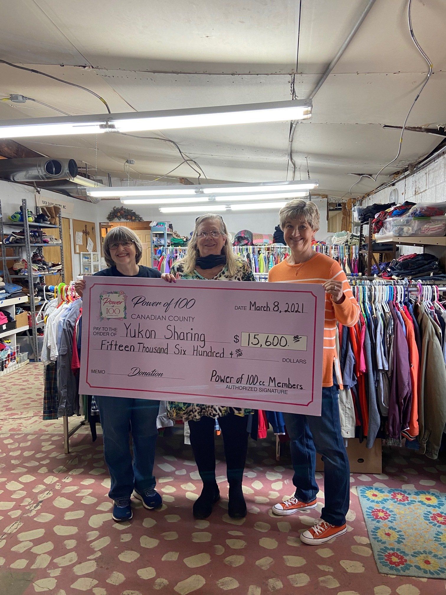 Three women are holding a large check in a store.