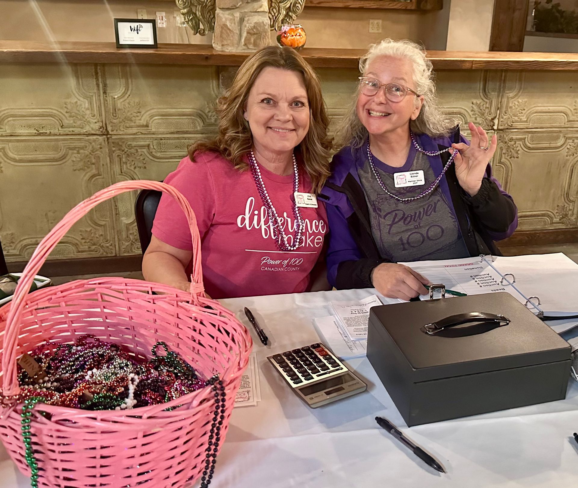 Two women are sitting at a table with a basket of beads.