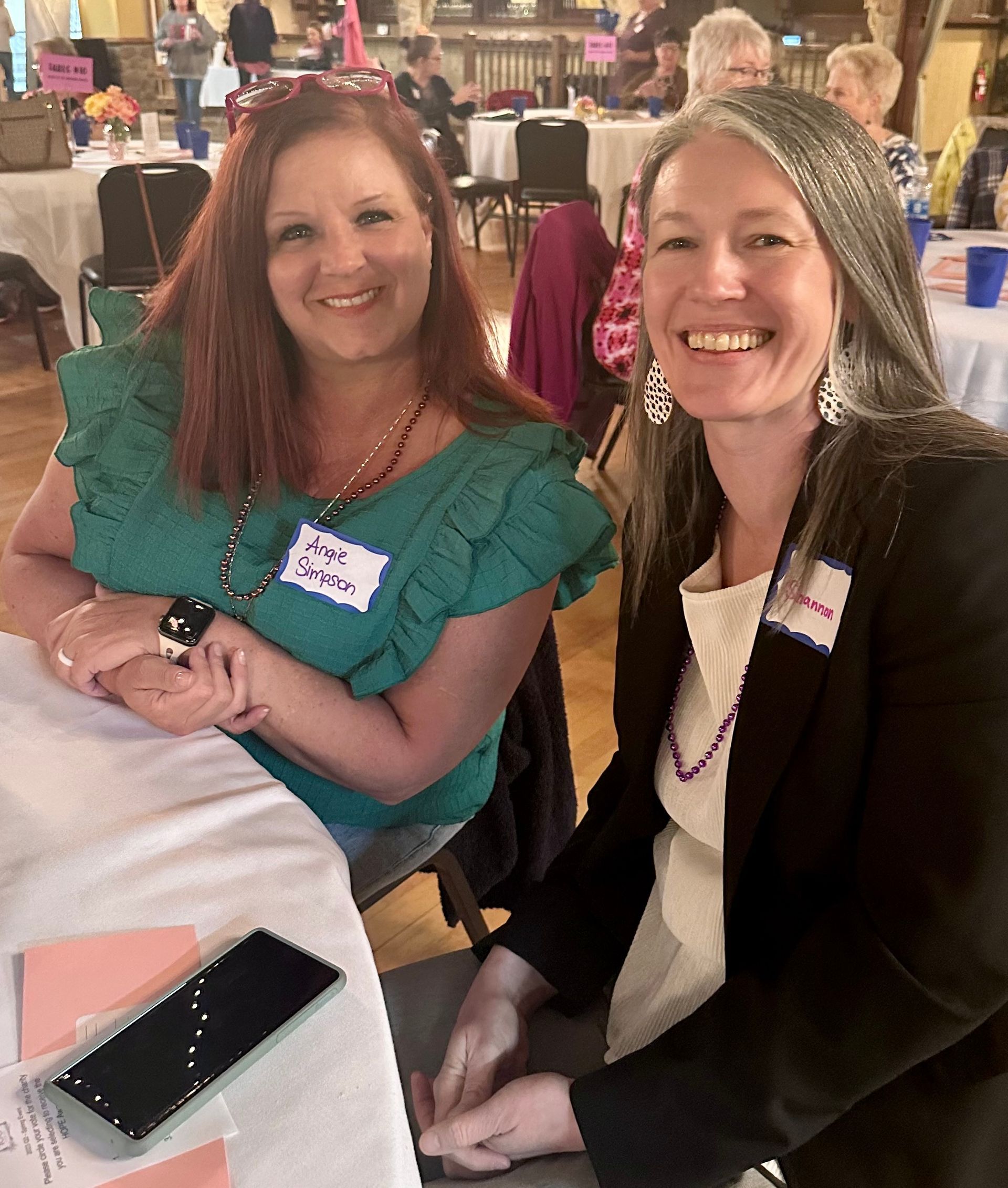 Two women are sitting at a table and one has a name tag that says mary singer