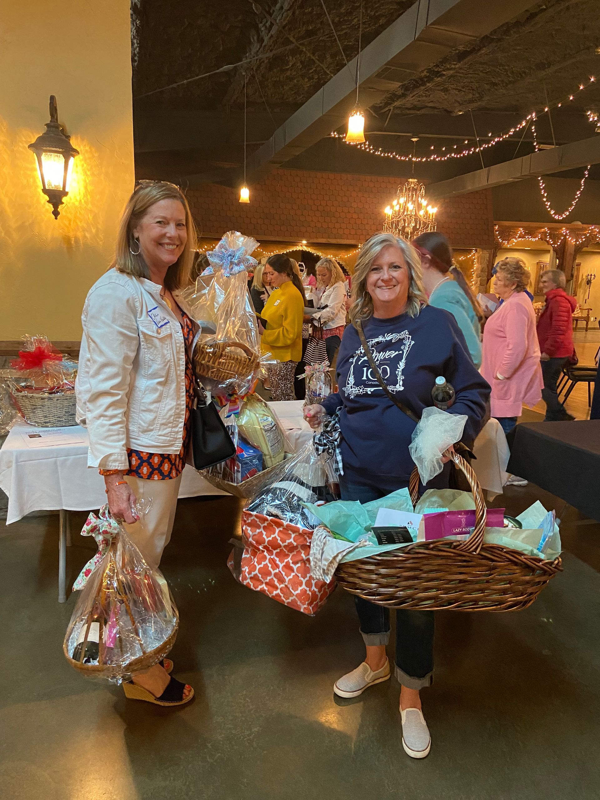 Two women are standing next to each other in a room holding baskets.