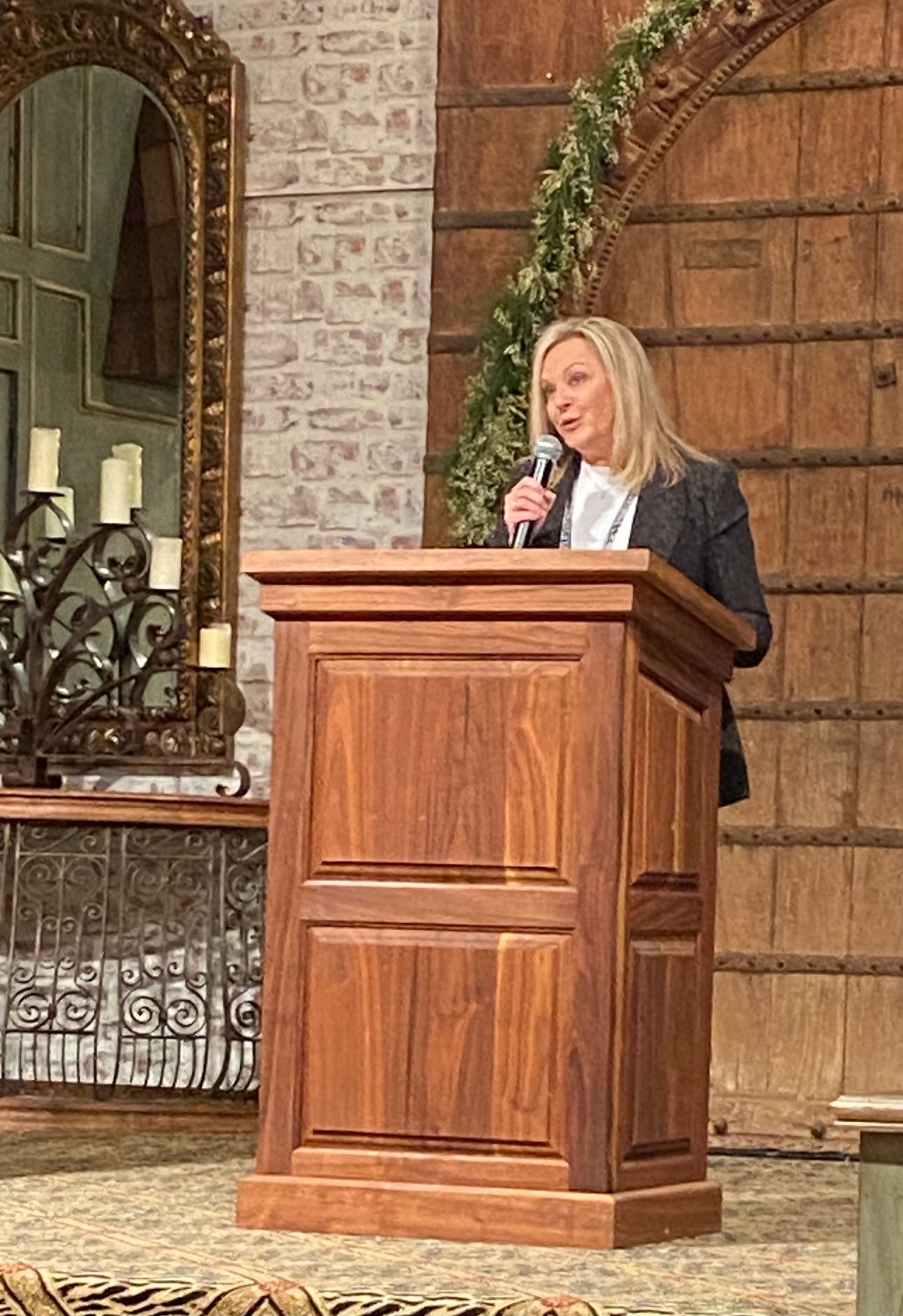 A woman is standing at a wooden podium holding a microphone.