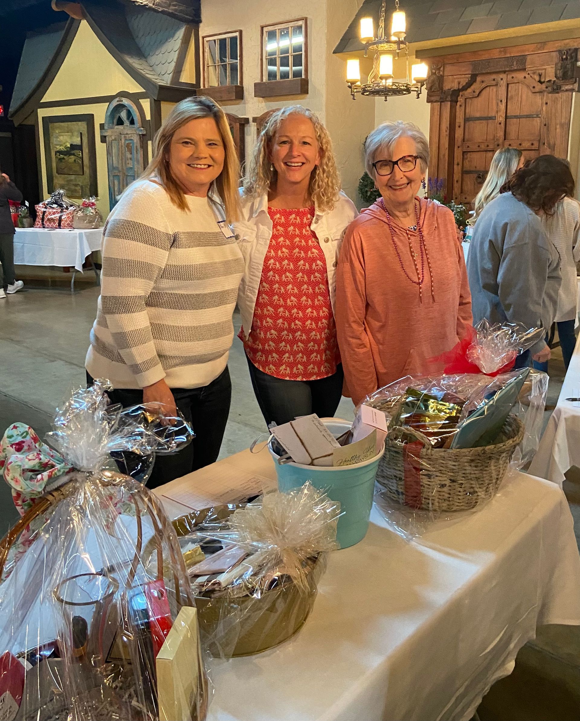 Three women are posing for a picture in front of a table filled with baskets.