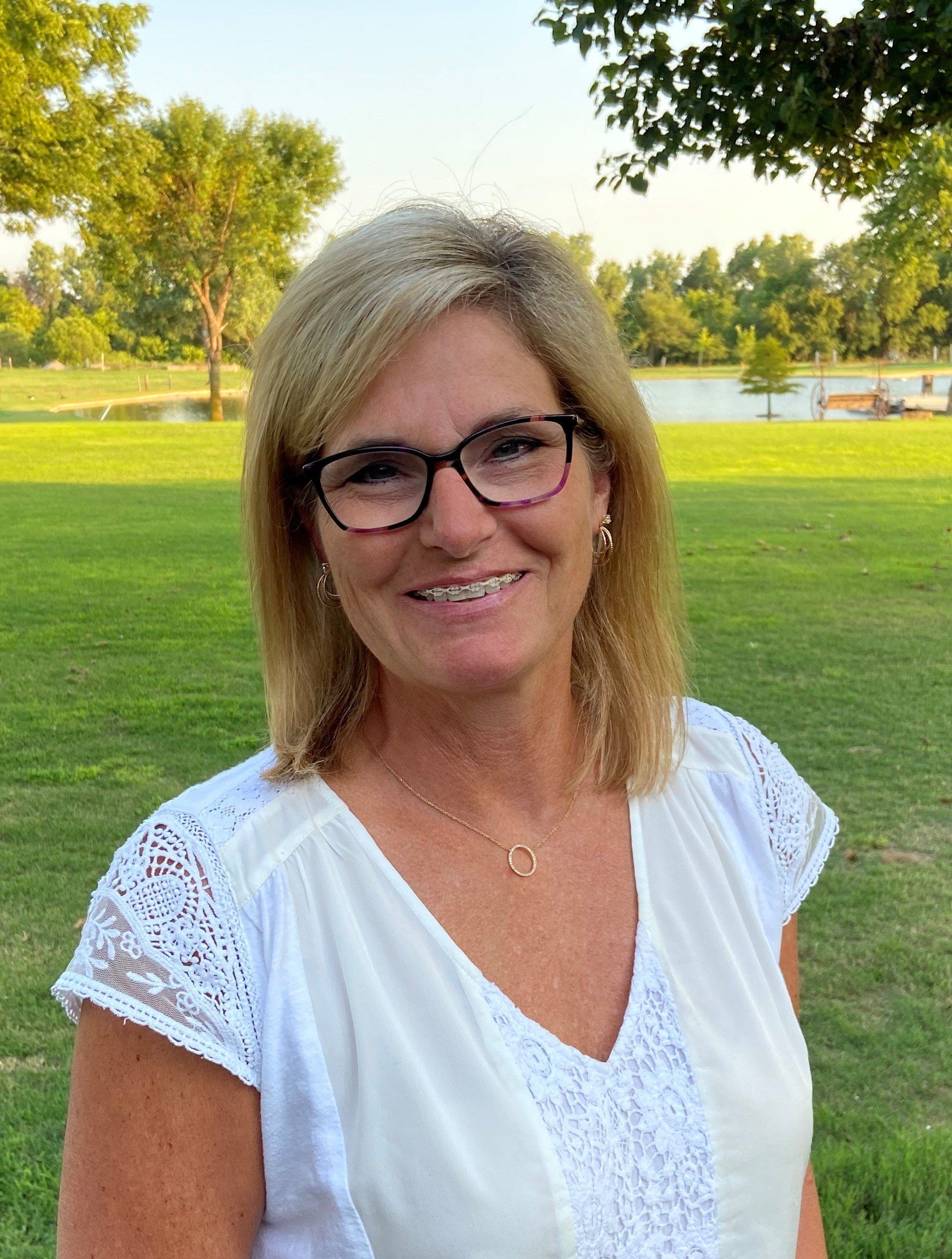 A woman wearing glasses and a white shirt is standing in a park.